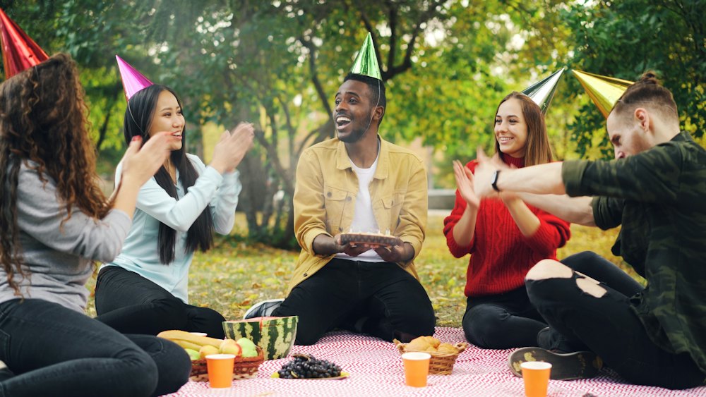 Friends in party hats celebrating a birthday with cake outdoors